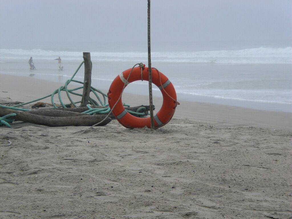 Plage d’Assouindé avec une bouée de sauvetage orange accrochée à un poteau et des vagues au loin