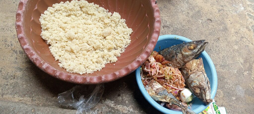 Attiéké dans un plat en terre cuite servi avec du poisson fumé et du piment