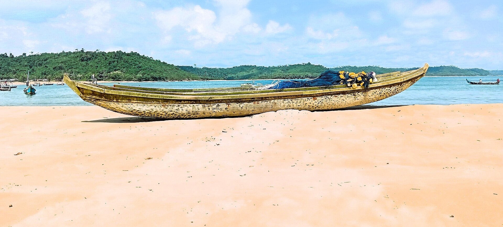 Pirogue peinte posée sur une plage de sable clair du Bas-Sassandra, face à une baie bordée de collines boisées