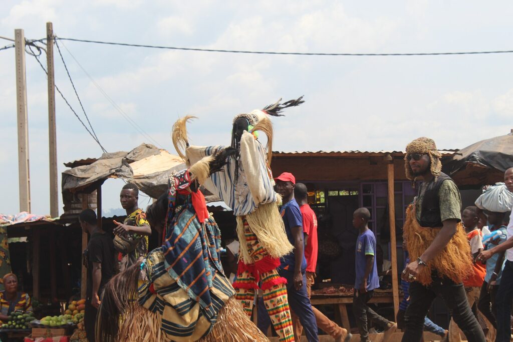 Danseur portant un grand masque à plumes lors d’une sortie de masque dans une rue de Man, entouré de spectateurs
