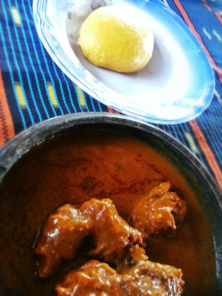 Boule de foutou banane posée dans une assiette à côté d'un bol de sauce graine avec de la viande