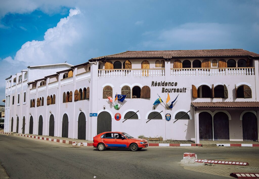 Façade blanche à arcades d’inspiration coloniale dans le quartier France de Grand-Bassam, un taxi orange garé devant