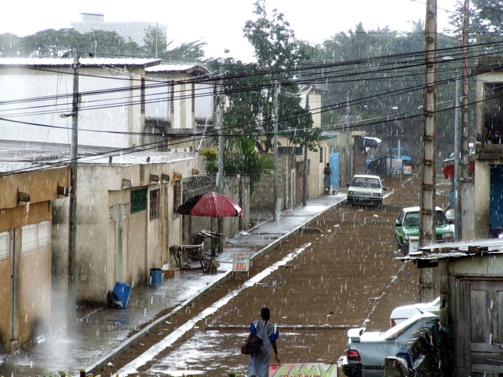 Rue de Yopougon à Abidjan sous une pluie battante, chaussée mouillée et câbles électriques