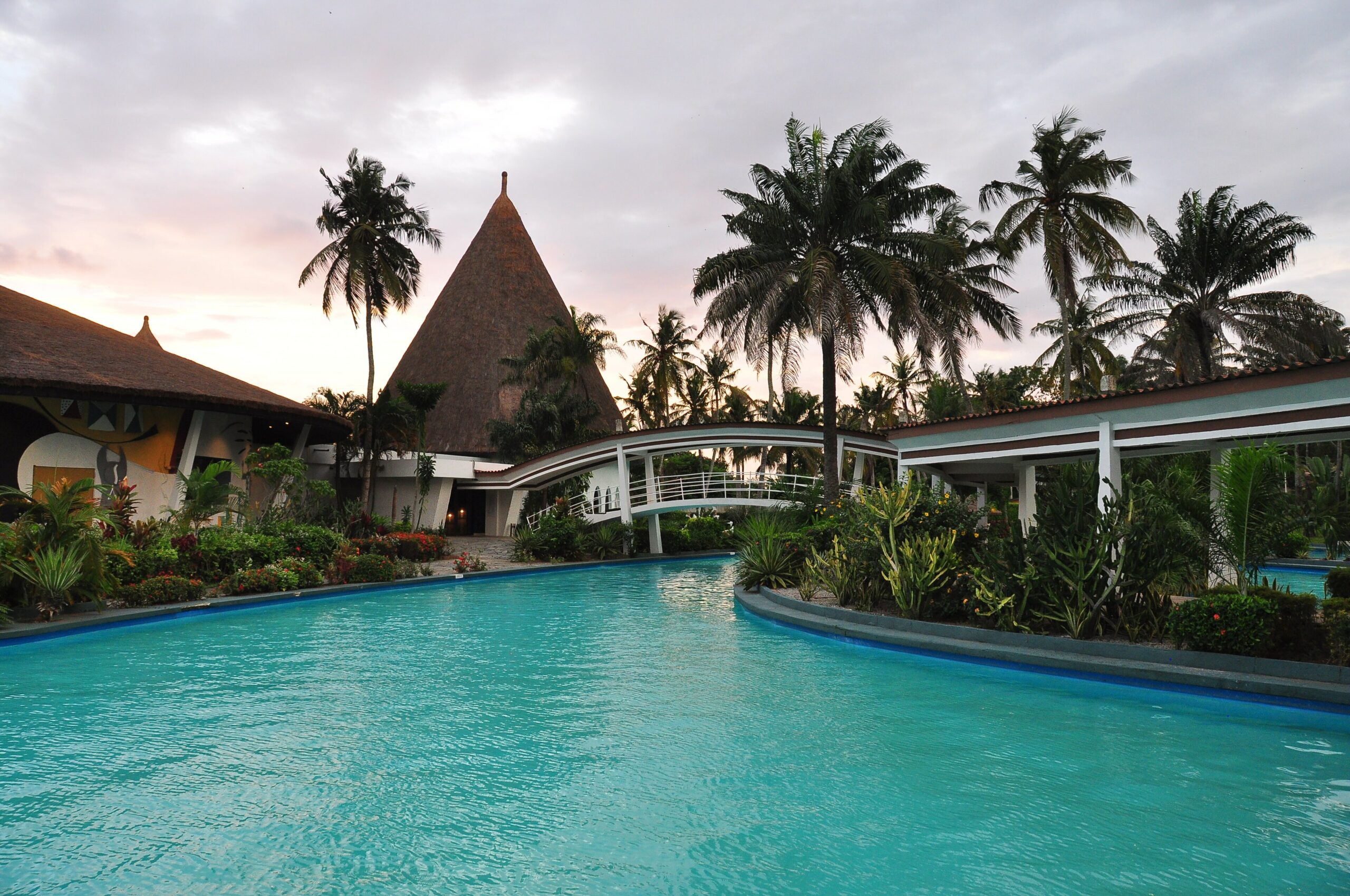 Paillote au toit pointu et piscine bordée de palmiers à l'Hôtel Ivoire d'Abidjan