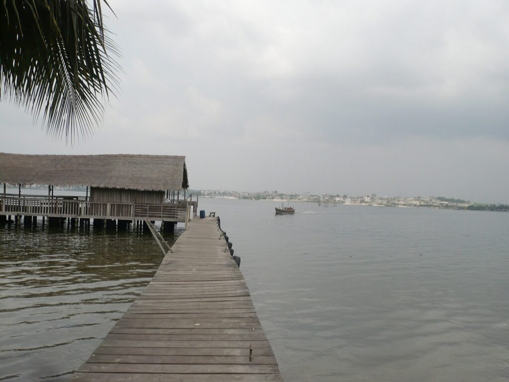 Ponton en bois s’avançant sur la lagune Ébrié depuis l’île Boulay, avec des paillotes au bord de l’eau