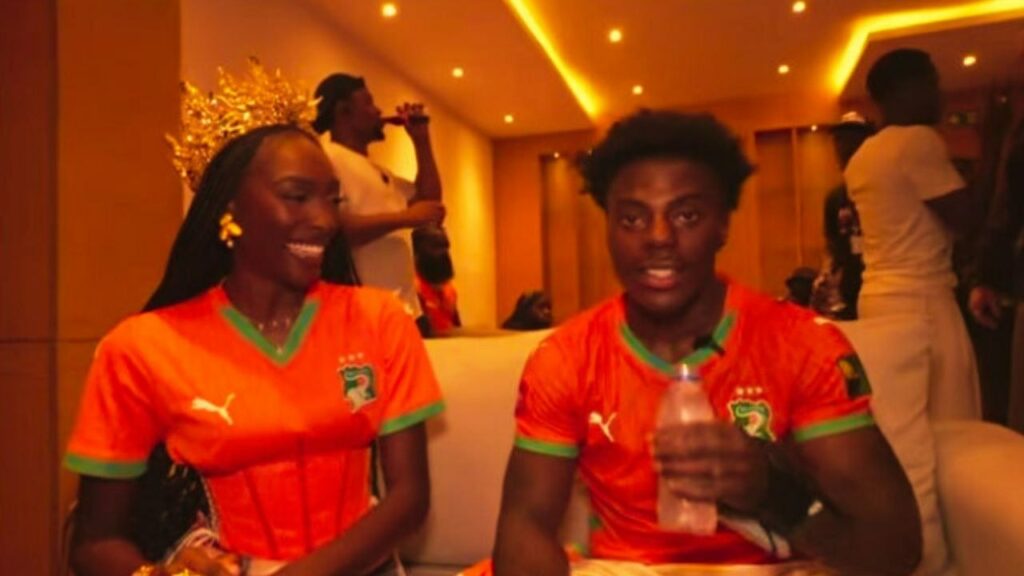 IShowSpeed en maillot orange des Éléphants, assis à côté d'une jeune femme couronnée, pendant une interview