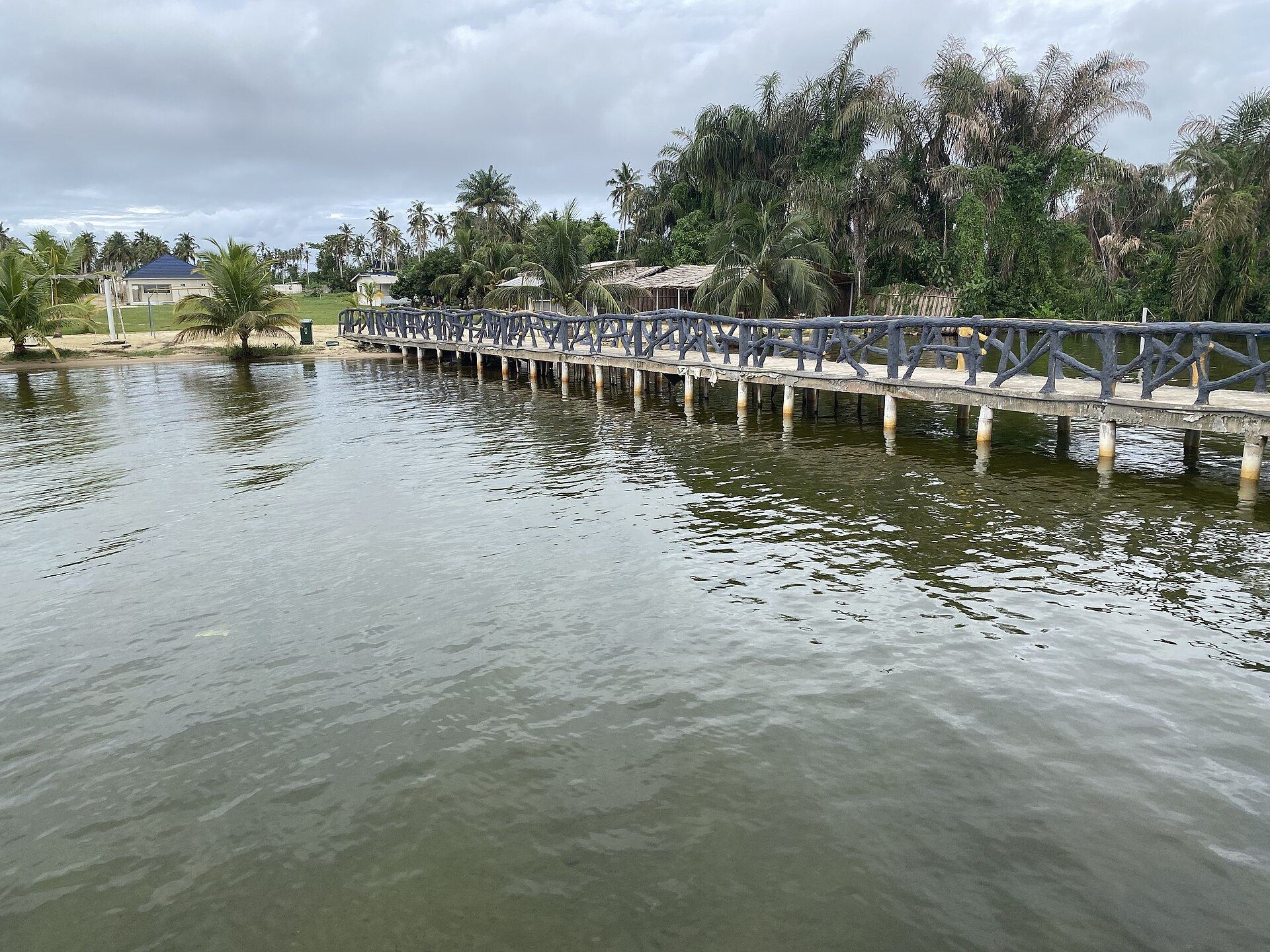 Long ponton de bois sur la lagune Ébrié à Jacqueville, bordé de cocotiers et de jardins