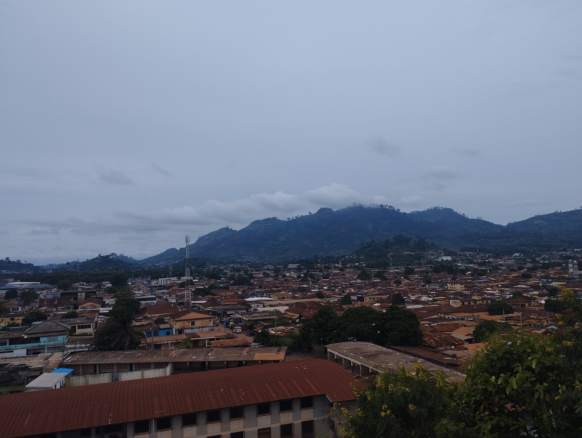 Vue panoramique de Man, ses toits et ses quartiers au pied d’une chaîne de montagnes boisées