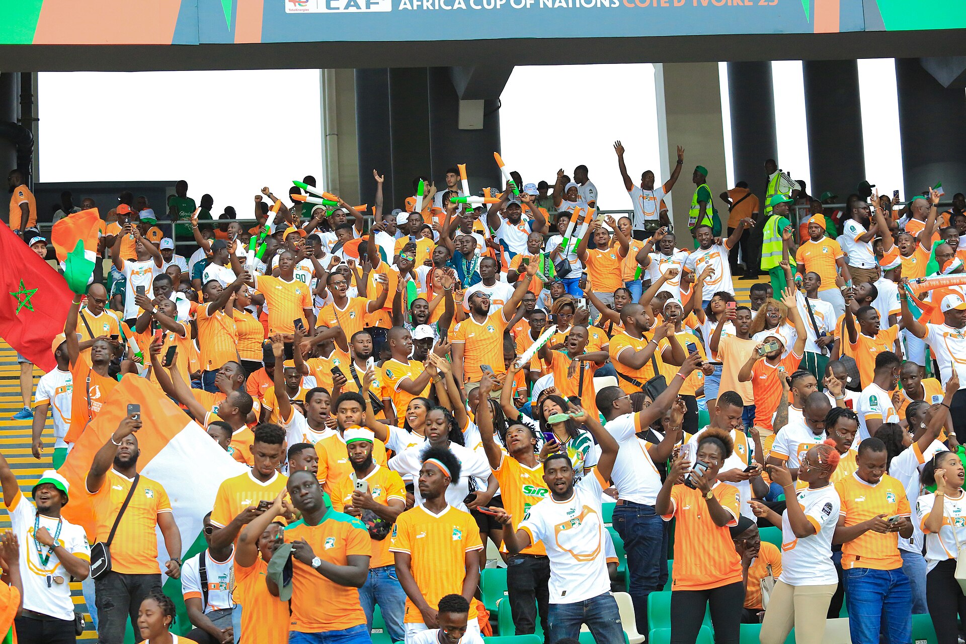 Tribune remplie de supporters ivoiriens en orange, blanc et vert agitant des drapeaux lors du match d’ouverture de la CAN 2023
